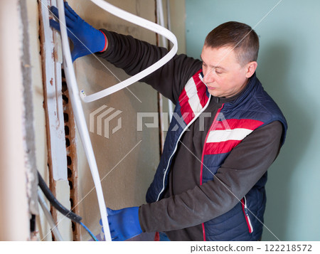 Plumber installs new plastic pipes in special boxes in the wall in house under construction 122218572