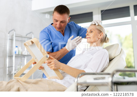 Mature woman sitting with mirror and discussing with male doctor for rejuvenation procedure Mature woman sitting with mirror and discussing with male doctor for rejuvenation procedure 122218578