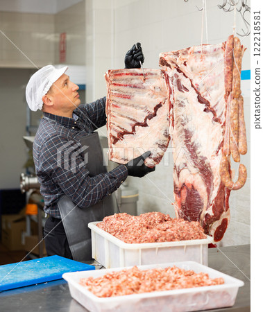 Diligent male butcher showing big piece of beef ribs in meat section of supermarket Diligent male butcher showing big piece of beef ribs in meat section of supermarket 122218581