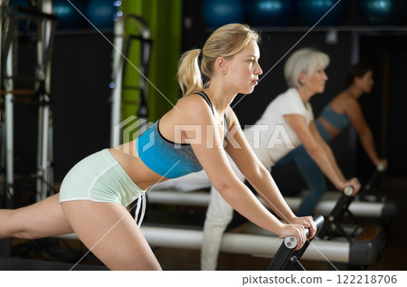 Young woman standing on pilates reformer, perform exercises 122218706
