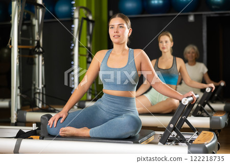 Girl sitting on foldable bed reformer performs exercises, strengthening body and muscles 122218735