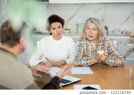 Two women sitting at the kitchen-table face to face with male agent 122218740