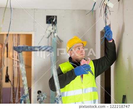 Electrician mounting electrical wiring inside building in process of construction Electrician mounting electrical wiring inside building in process of construction 122218747