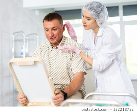 Satisfied middle-aged man patient holding mirror sitting on clinical chair 122218752
