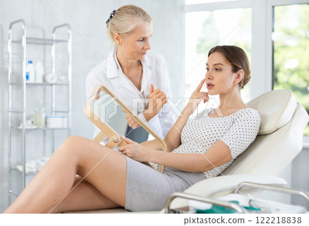 Elderly female plastic surgeon showing results of facial procedure to woman Elderly female plastic surgeon showing results of facial procedure to woman 122218838