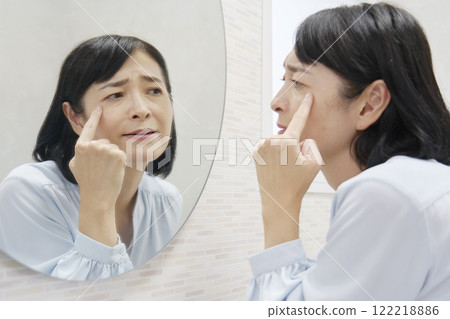 A woman in her 50s worries about the corners of her eyes in the mirror 122218886