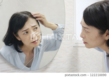 A woman in her 50s looking in the mirror and worrying about her gray hair A woman in her 50s looking in the mirror and worrying about her gray hair 122218890
