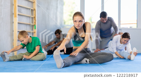 Family in gym during group sports training under guidance of trainer performs stretching on floor Family in gym during group sports training under guidance of trainer performs stretching on floor 122218917