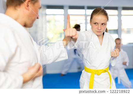 Teen girl at group training in gym practice karate punch block technique with trainer Teen girl at group training in gym practice karate punch block technique with trainer 122218922