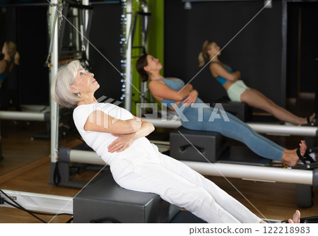 Woman sitting on reformer and bending over Woman sitting on reformer and bending over 122218983