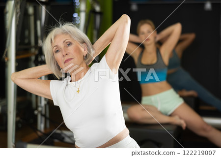 Senior woman sitting on box set equipment reformer performs for abdominal muscles, close up Senior woman sitting on box set equipment reformer performs for abdominal muscles, close up 122219007