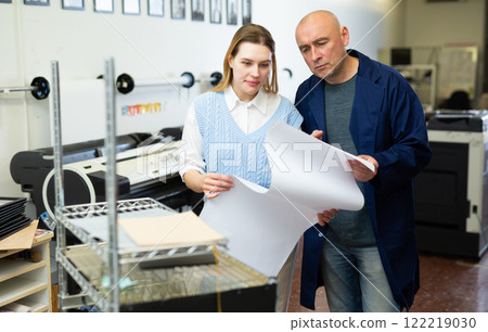 Woman and man checking large format paper after printing 122219030
