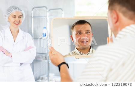 Satisfied man examines his face in mirror after plastic surgery Satisfied man examines his face in mirror after plastic surgery 122219078