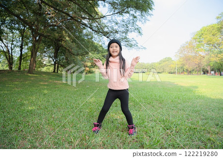 A young girl joyfully plays outdoors on a sunny day in a green park. 122219280