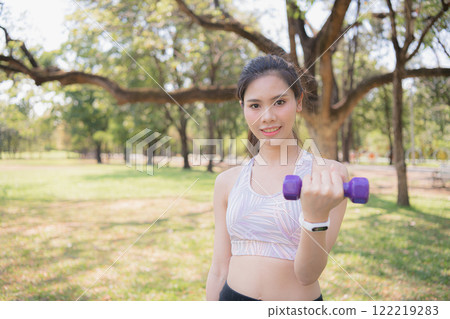 A young woman holding a dumbbell in a lush park, promoting fitness and wellness. 122219283