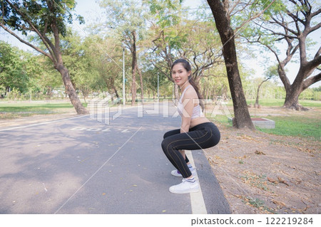 A young woman performing exercise outdoors in a park. 122219284