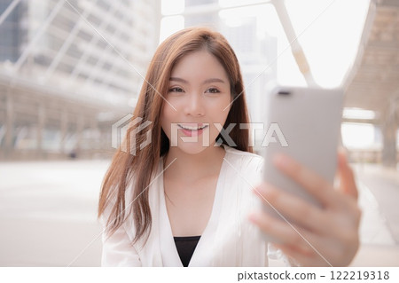A young woman smiling while taking a selfie in an urban setting. A young woman smiling while taking a selfie in an urban setting. 122219318