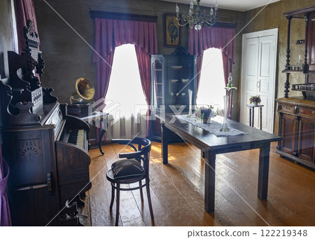 Restored interior of an early 20th century house with a piano, gramophone and a cupboard for dishes 122219348
