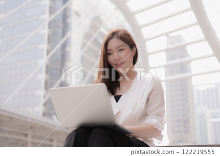 A professional woman engaged in work on a laptop in a modern urban environment. A professional woman engaged in work on a laptop in a modern urban environment. 122219555