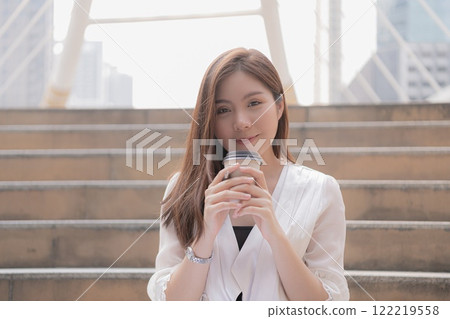A woman enjoys a drink while sitting on steps in an urban setting. A woman enjoys a drink while sitting on steps in an urban setting. 122219558