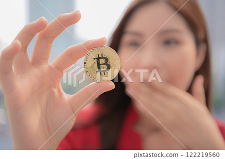 A woman holding a Bitcoin with a surprised expression against a city backdrop. A woman holding a Bitcoin with a surprised expression against a city backdrop. 122219560