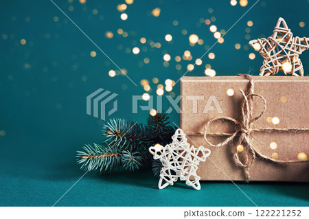 Festive gift box with pine branch and stars on teal background with bokeh lights Festive gift box with pine branch and stars on teal background with bokeh lights 122221252