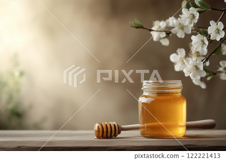 Natural honey in a jar with a dipper beside delicate white blossoms 122221413