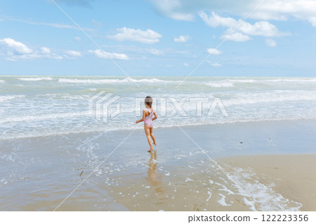 rea view of little girl in the swimsuit jumping on the beach playing with waves 122223356