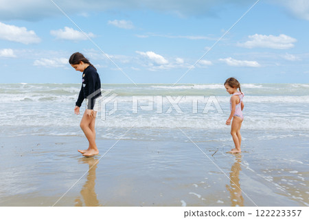 side view of little girls in the swimsuit standing on the beach playing with waves 122223357