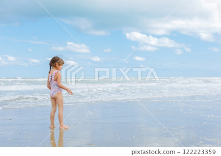 side view of little girl in the swimsuit standing on the beach playing with waves side view of little girl in the swimsuit standing on the beach playing with waves 122223359