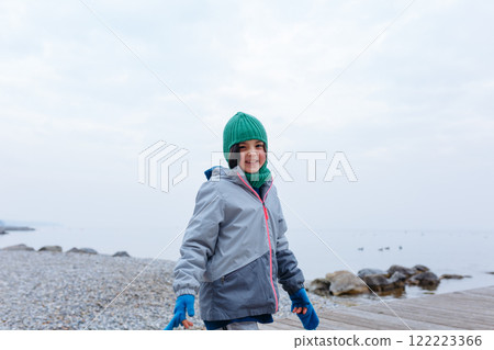 smiling girl in green winter baclava standing in front of the lake 122223366