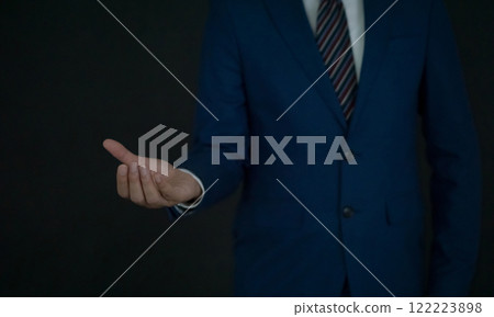 A businessman dressed in a blue formal suit standing with his hand open and facing up, conveying professionalism and engagement in a corporate environment. A businessman dressed in a blue formal suit standing with his hand open and facing up, conveying professionalism and engagement in a corporate environment. 122223898