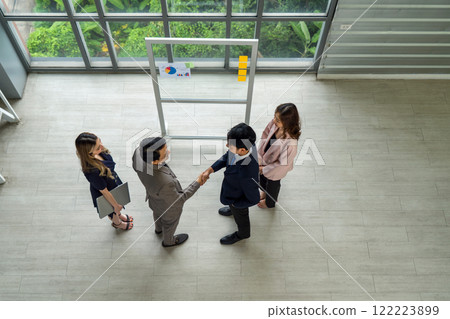 Business partners shaking hands in front of a large glass window, displaying unity and ambition in their workplace. 122223899