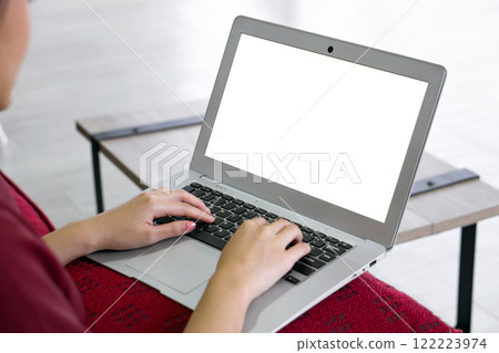 Back view of businesswoman in red dress working at home. Laptop computer and cushion are on her lap. 122223974