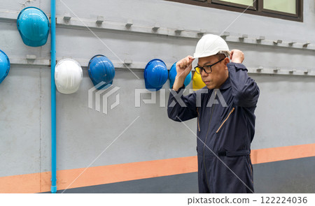 Asian man in mechanic coverall dust protection suit, wearing construction hardhat on his head for safety. Concept of work safety. Building industry. 122224036