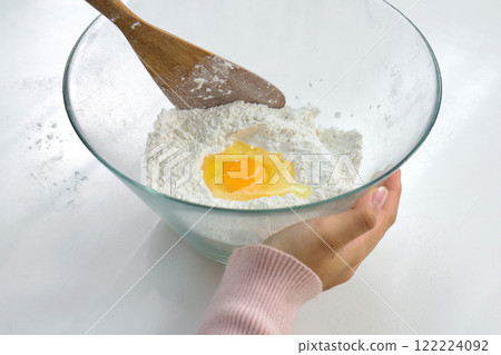 Closeup hand holding glass bowl with an egg and flour, preparing to bake. Closeup hand holding glass bowl with an egg and flour, preparing to bake. 122224092