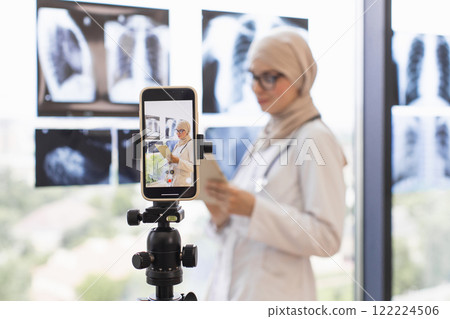 Young Muslim woman doctor records medical lesson using x-ray images on smartphone. Focus on education, professional development in healthcare setting with technology. Young Muslim woman doctor records medical lesson using x-ray images on smartphone. Focus on education, professional development in healthcare setting with technology. 122224506