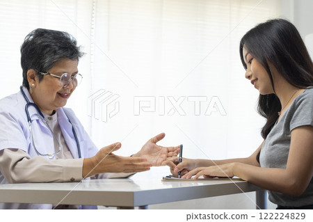 General practitioner taking notes when talking to female patient in hospital. 122224829