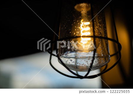 Vintage light bulb glowing brightly in a cozy setting, creating a warm atmosphere during the evening hours Vintage light bulb glowing brightly in a cozy setting, creating a warm atmosphere during the evening hours 122225035