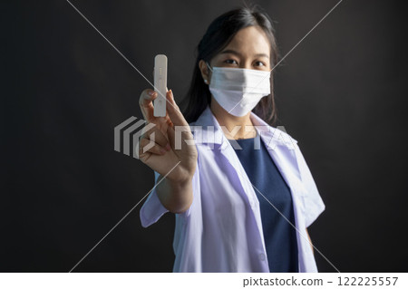 Young asian female doctor holding ATK kit standing on black background. Young asian female doctor holding ATK kit standing on black background. 122225557