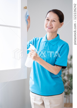 Senior female housekeeper cleaning windows 122226242