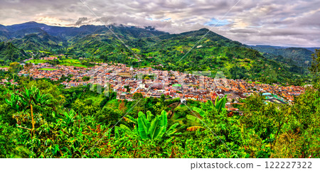 Sunrise panorama of Jardin, a charming colonial town in Colombia, surrounded by lush green mountains, dense tropical vegetation, and dramatic skies 122227322