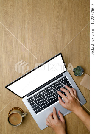 Overhead view of hands typing on laptop keyboard at minimalist desk with a coffee cup and a small plant 122227669