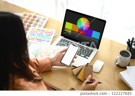 Interior designer holding smartphone reviewing design sketches and wooden material samples Interior designer holding smartphone reviewing design sketches and wooden material samples 122227685