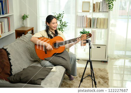 Smiling woman playing acoustic guitar and recording video content for social media with smartphone 122227687
