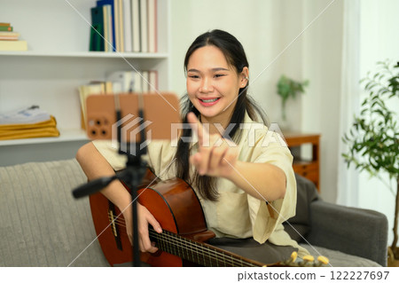 Smiling woman playing acoustic guitar and recording video content for social media with smartphone 122227697