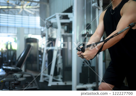 Determined man working out in a gym with a cable machine. Sports and healthy lifestyle concept Determined man working out in a gym with a cable machine. Sports and healthy lifestyle concept 122227700