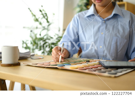 Female interior designer sketching and selecting materials for a home renovation project at desk 122227704