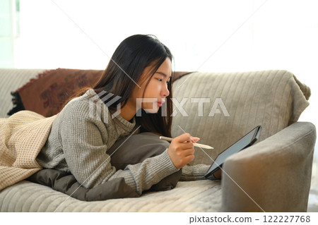 Young woman lying comfortably on the couch and using digital tablet with a stylus pen 122227768