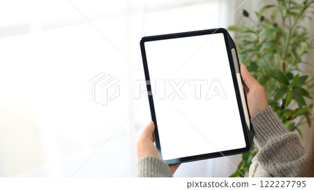 Close up of woman holding digital tablet with empty screen sitting in living room Close up of woman holding digital tablet with empty screen sitting in living room 122227795